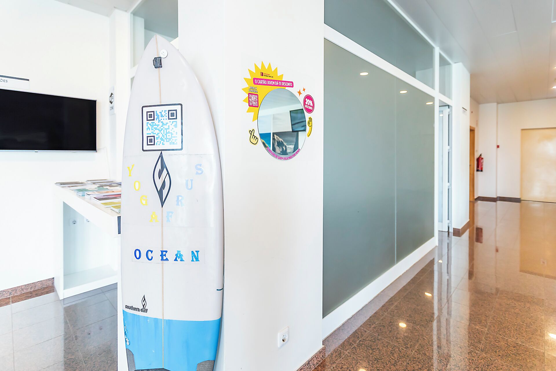 A hallway with a surfboard, a wall with a QR code, and a fire extinguisher.