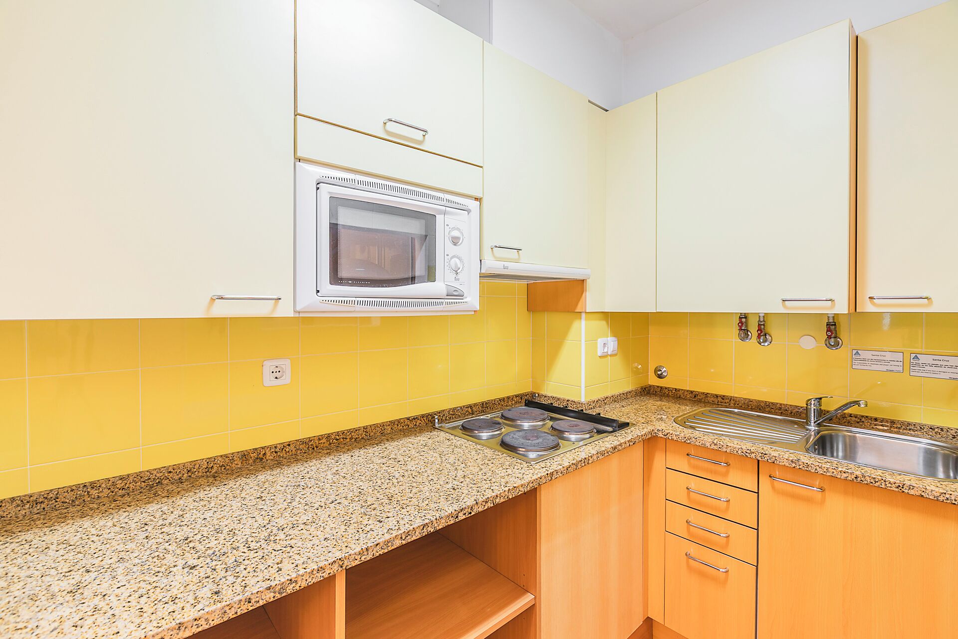 A kitchen with yellow cabinets, a built-in oven, a granite countertop, and a stainless steel sink.