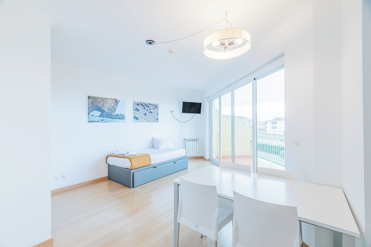 Una habitación de hotel moderna con cama, escritorio, silla, televisor y ventanas amplias.