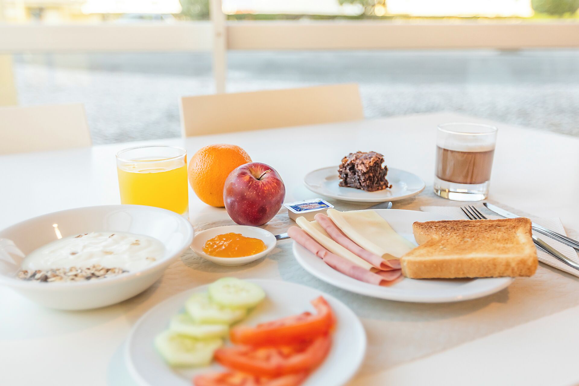 A breakfast table with various food items, a glass of juice, and a cup of coffee.