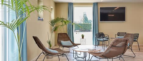 A modern lounge area with wicker chairs, a coffee table, and a large TV screen.