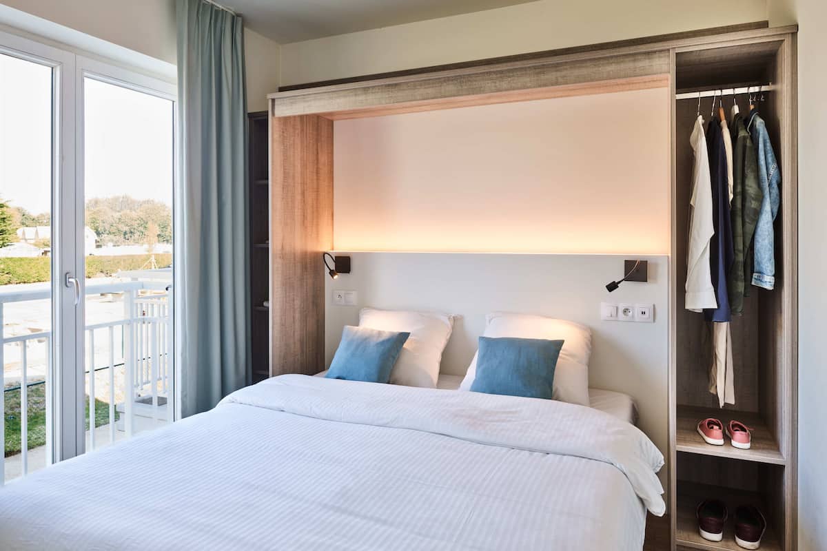 Habitación de hotel con cama, armario y balcón con vistas.