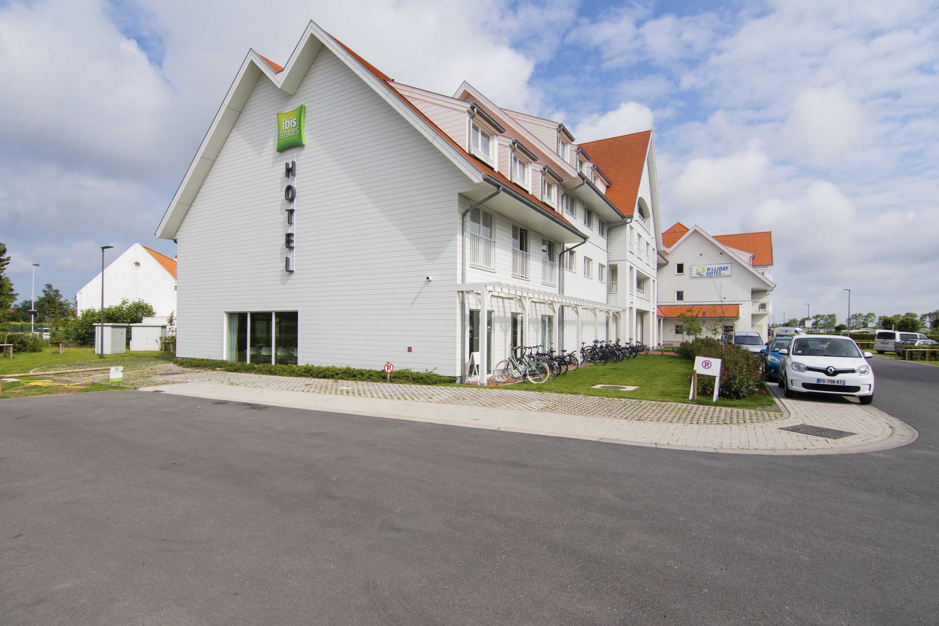 Ein modernes Hotel mit auffälliger Beschilderung, einem überdachten Bereich für Fahrräder und einem Parkplatz.