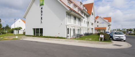 Ein modernes Hotel mit auffälliger Beschilderung, einem überdachten Bereich für Fahrräder und einem Parkplatz.
