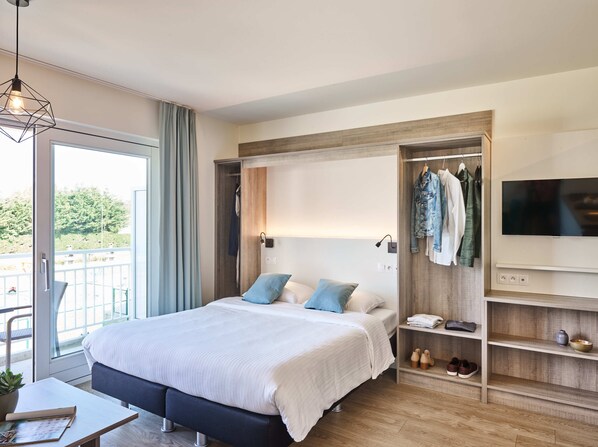 A modern hotel room with a large bed, a TV mounted on the wall, a wardrobe, and a balcony with a view of trees. - Holiday Suites Nieuwpoort (Nieuwpoort)