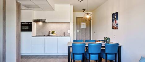 A modern kitchen with white cabinets, a built-in oven, and a dining area with blue chairs and a wooden table.