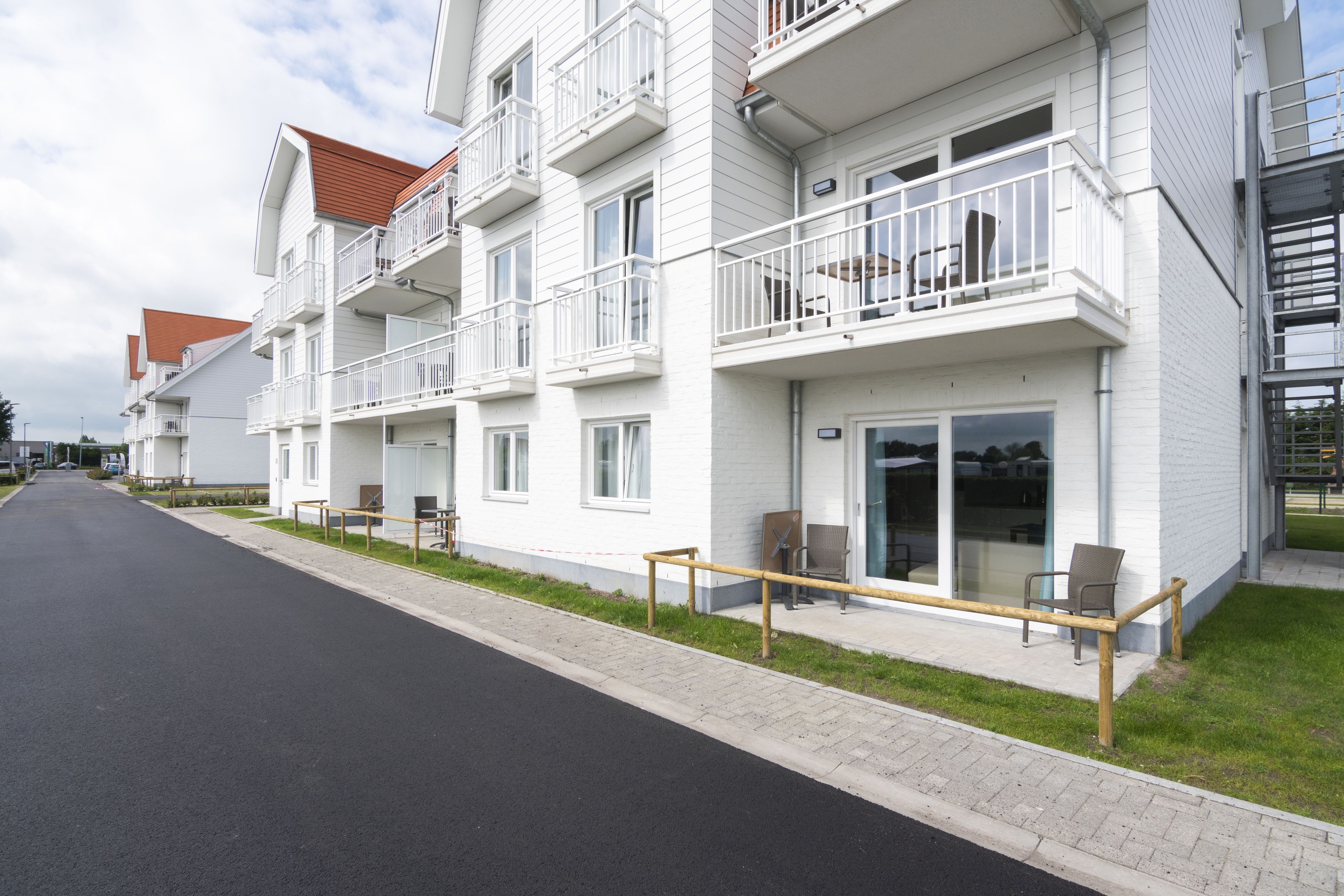 Um edifício residencial moderno com vários andares, varandas, calçada pavimentada e área de estar externa.