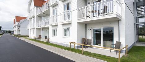 A modern multi-story residential building with balconies, a paved sidewalk, and outdoor seating.