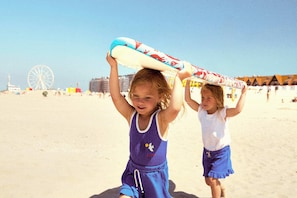 Dos niños en una playa arenosa, uno sosteniendo una tabla de surf.