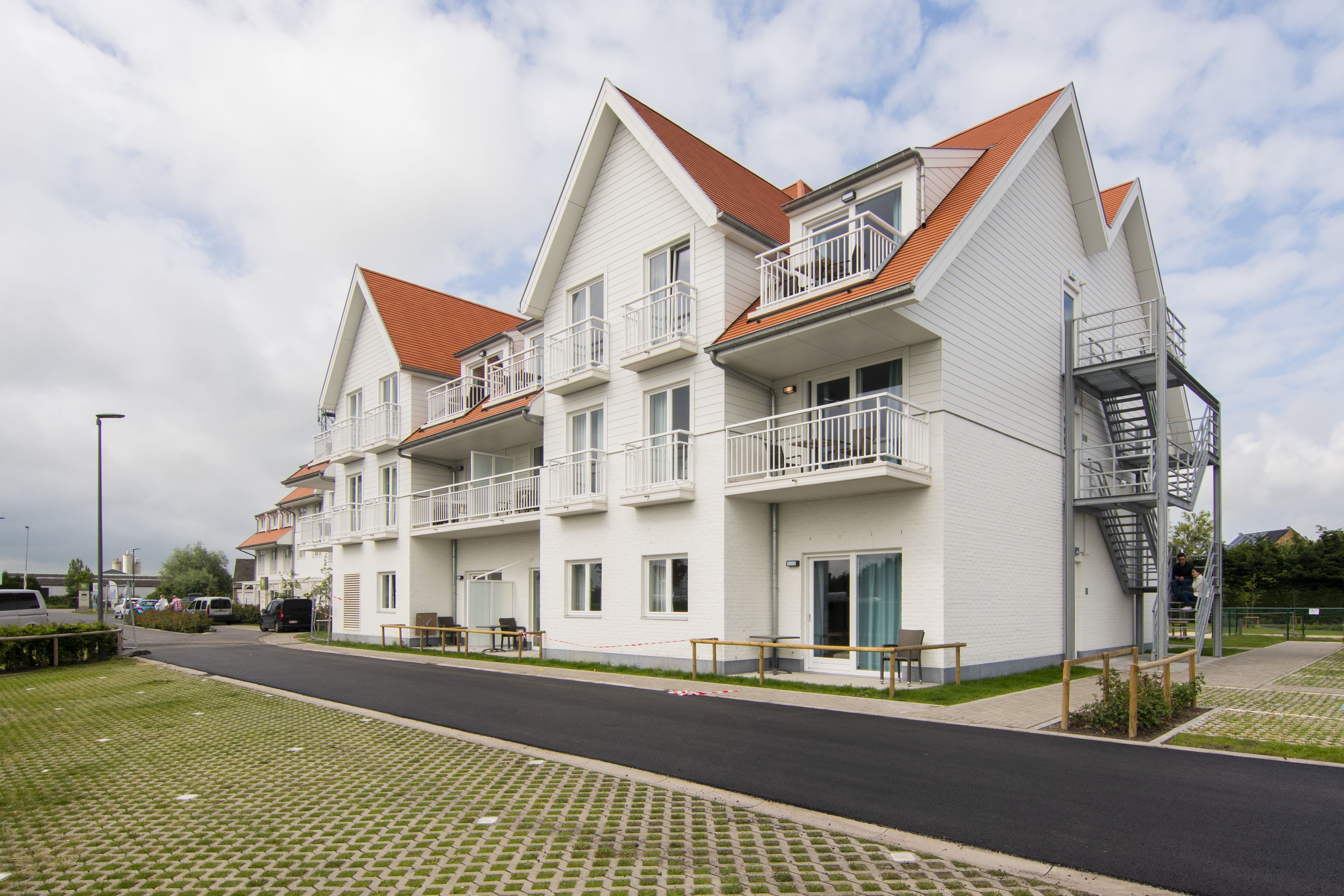 A multi-story residential building with balconies, a staircase, and a paved driveway.