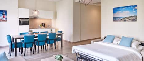A modern hotel room with a bed, a dining area, and a kitchenette.