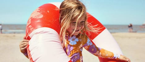 A person in a floral swimsuit holding a red and white inflatable lifeguard stand.
