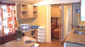 A compact kitchenette with a sink, a small TV, and a dining area with a table and chairs. - Villaggio Camping Orchidea (Grisolia)