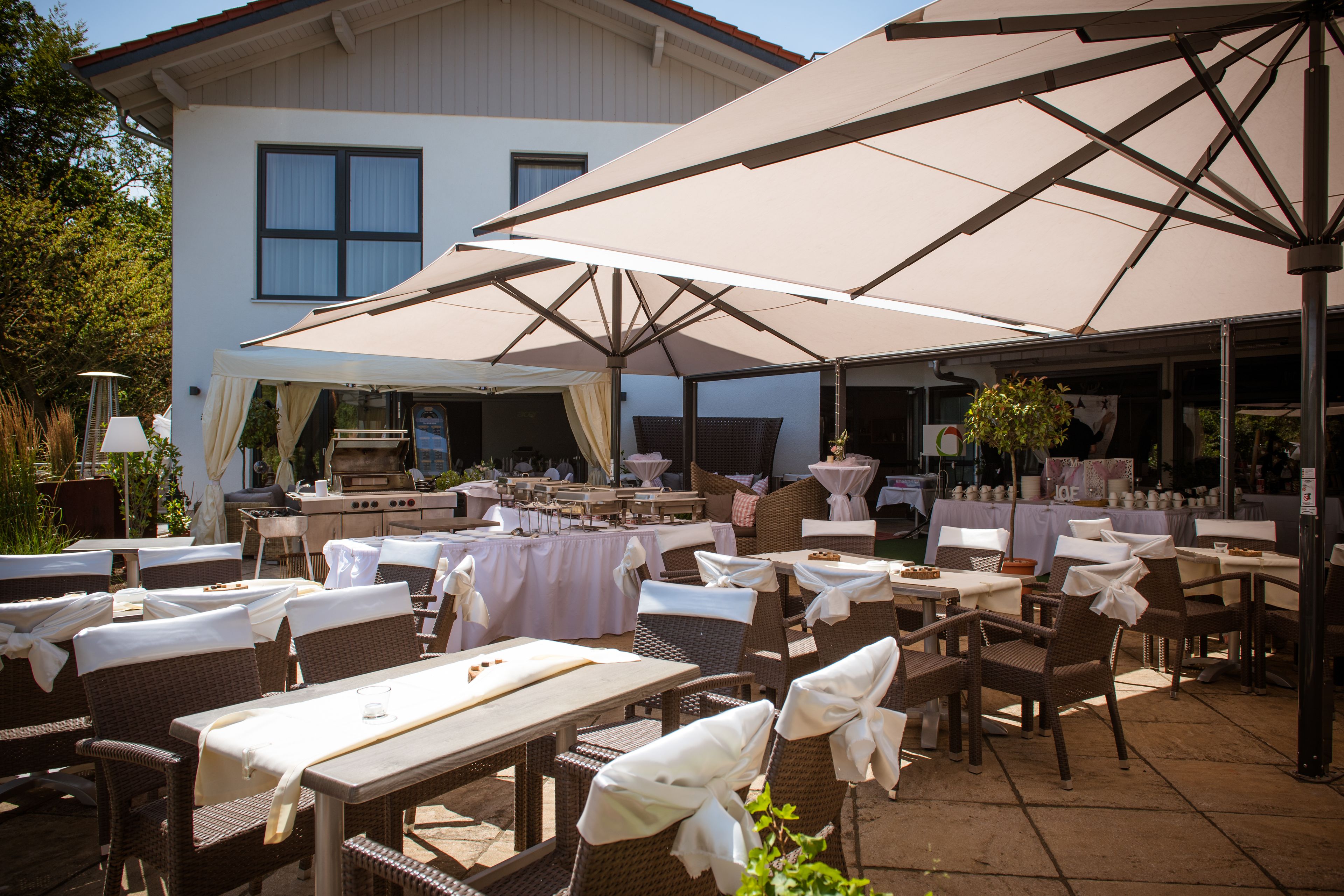 An outdoor patio area with tables and chairs, large umbrellas, and a grill.