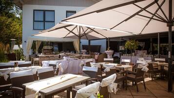 An outdoor patio area with tables and chairs, large umbrellas, and a grill.