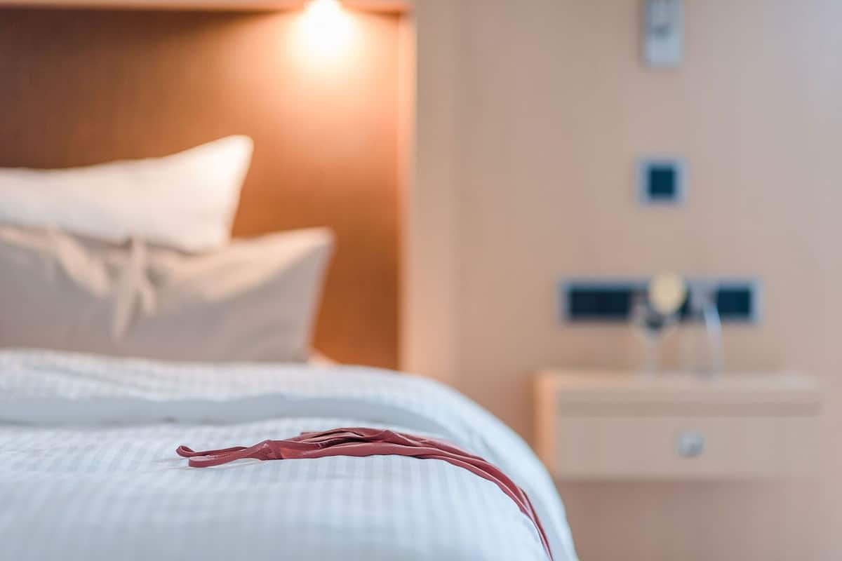 Una cama bien hecha con edredón blanco y un objeto rojo encima.