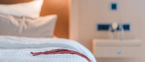 Una cama bien hecha con edredón blanco y un objeto rojo encima.