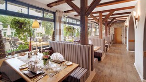 A restaurant with striped booths, wooden beams, and large windows overlooking a garden. - Romantik Hotel Ahrenberg (Bad Sooden-Allendorf)
