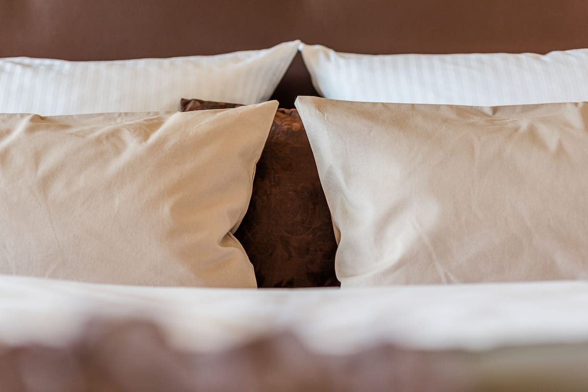 Una cama con sábanas blancas y una almohada marrón.
