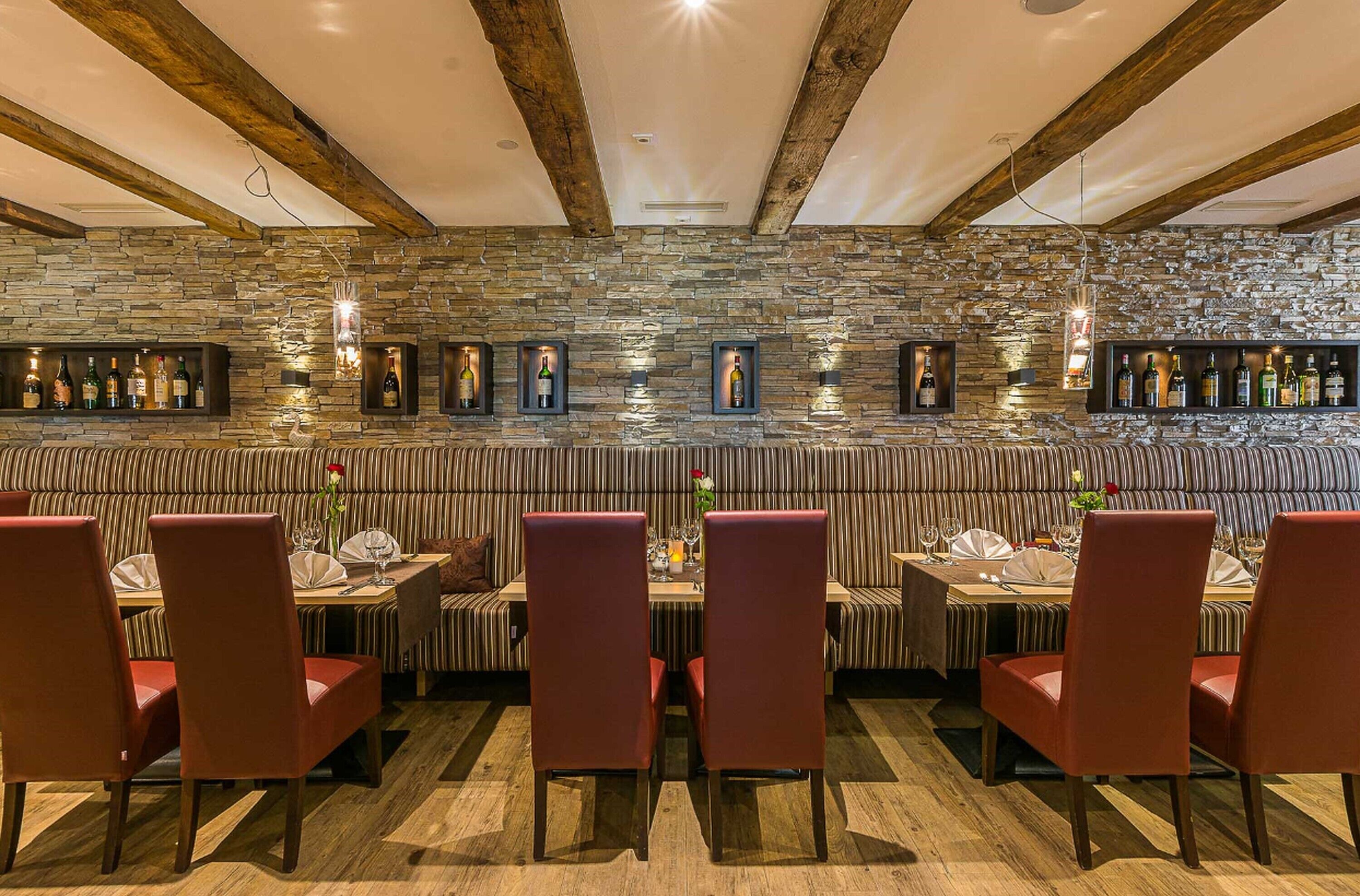Un restaurante con pared de piedra, vigas de madera y sillas rojas.