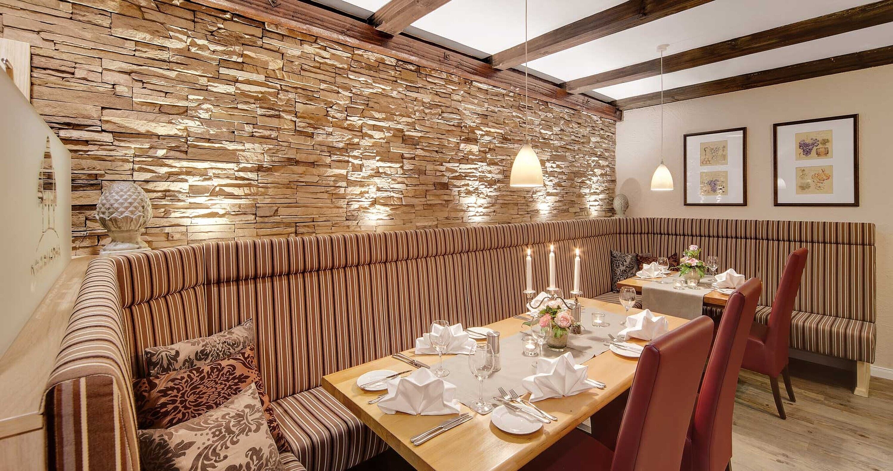 Un restaurante con pared de piedra, asientos a rayas y una mesa de madera dispuesta para comer.