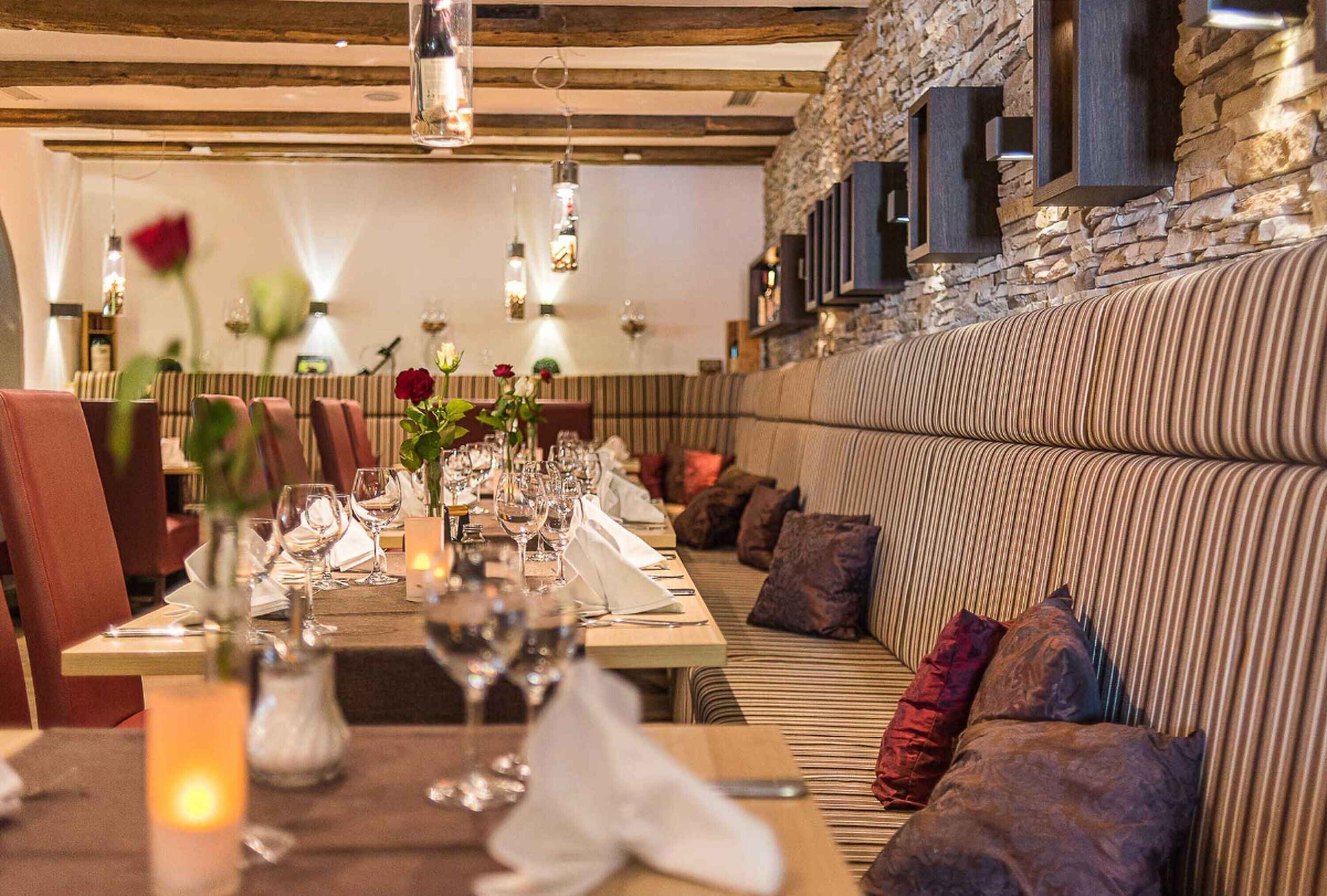 A restaurant with a long dining table set for a meal, cushioned seating, and a stone wall backdrop.