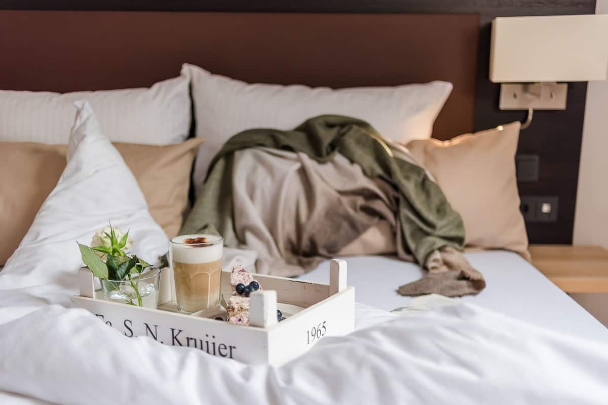Una cama bien tendida con una bandeja de desayuno que incluye una taza de café, un pequeño jarrón con flores y una vela.