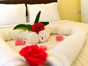 Cama bem arrumada com toalhas brancas dobradas e uma decoração de flor vermelha.