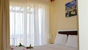 Habitación de hotel con cama, cortinas blancas, un cuadro en la pared y ventana con vistas.