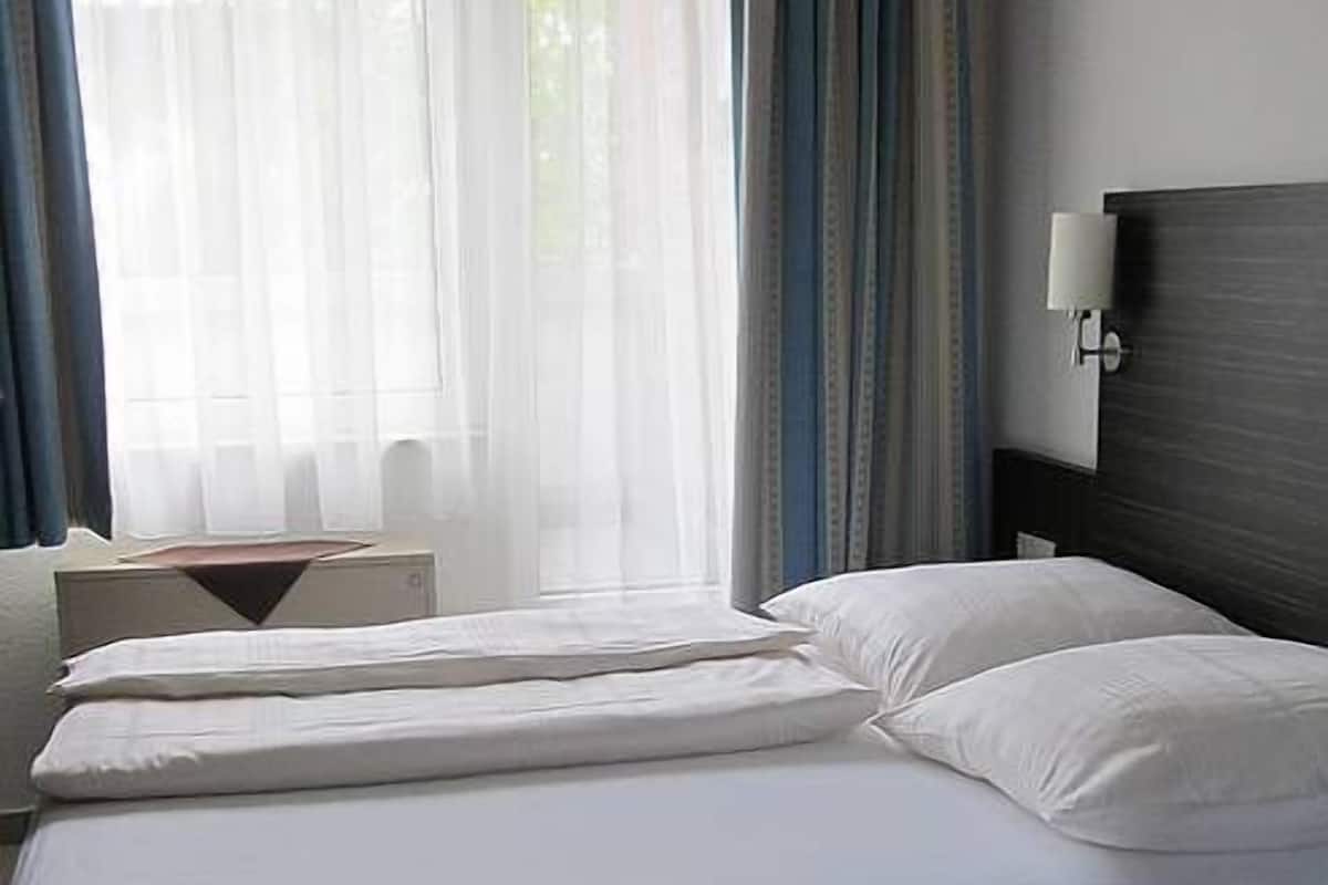 Un lit bien fait, avec du linge de lit blanc, une tête de lit sombre et un tapis bleu sur le sol.