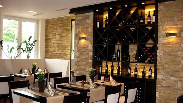 A restaurant interior with stone walls, a wine rack, and tables with chairs. - Hotel Konoba Restaurant - Bistro (Meckenheim)