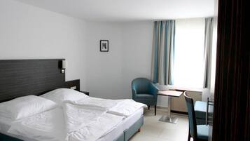 A hotel room with a bed, a desk, a chair, and a window with curtains.