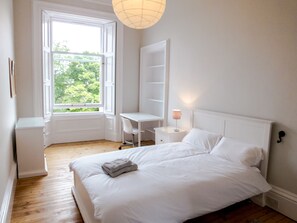 A bedroom with a bed, a desk, and a chair. There is a window with an open door, and a lamp on the nightstand. - Silver Lining - Luxury Thirlestane Road (Edinburgh)