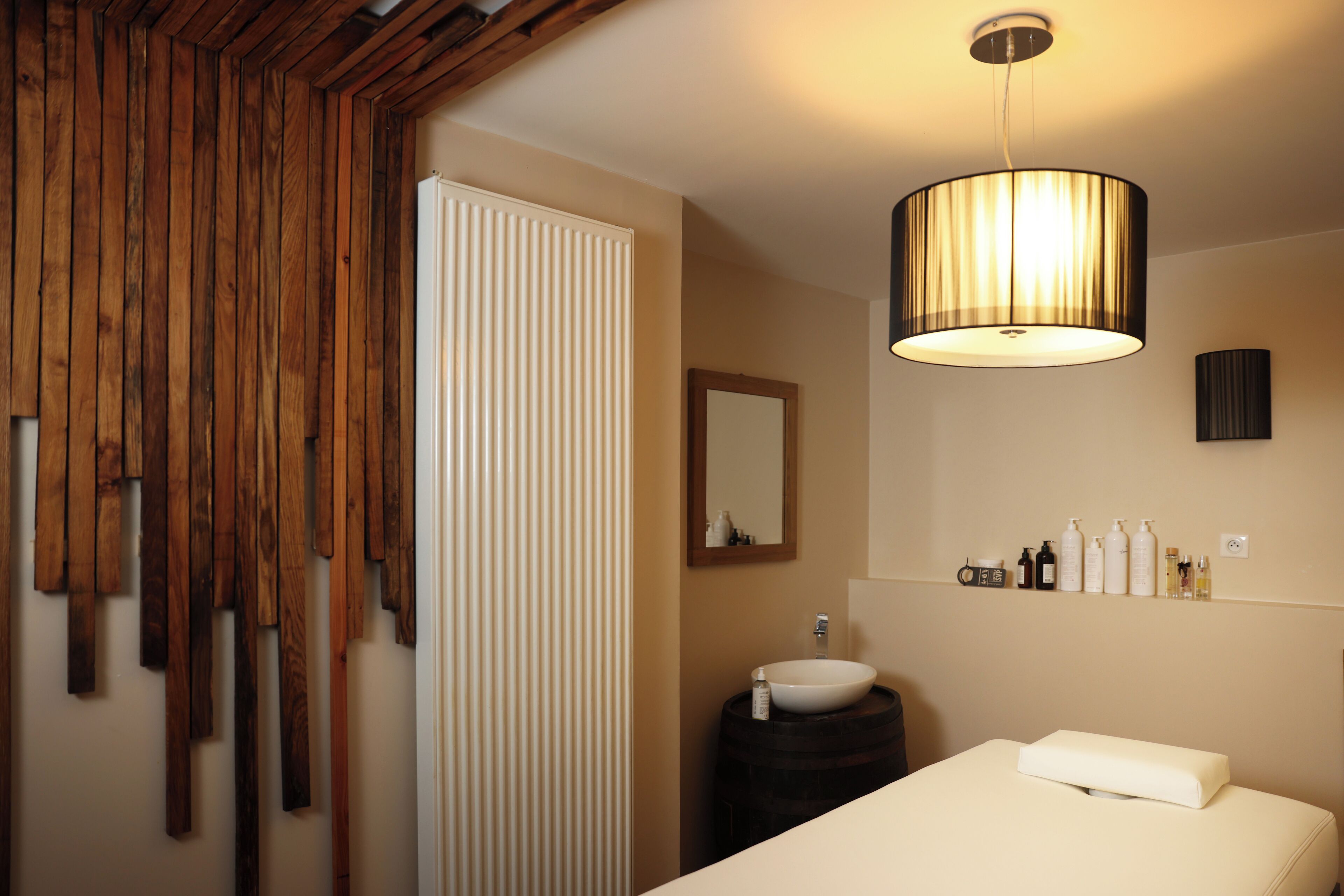 Een badkamer met een houten wandpaneel, een wit wastafeltje, een spiegel en een nachtkastje met een kussen.