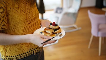 Iemand houdt een bord met pannenkoeken, bedekt met bessen en siroop.