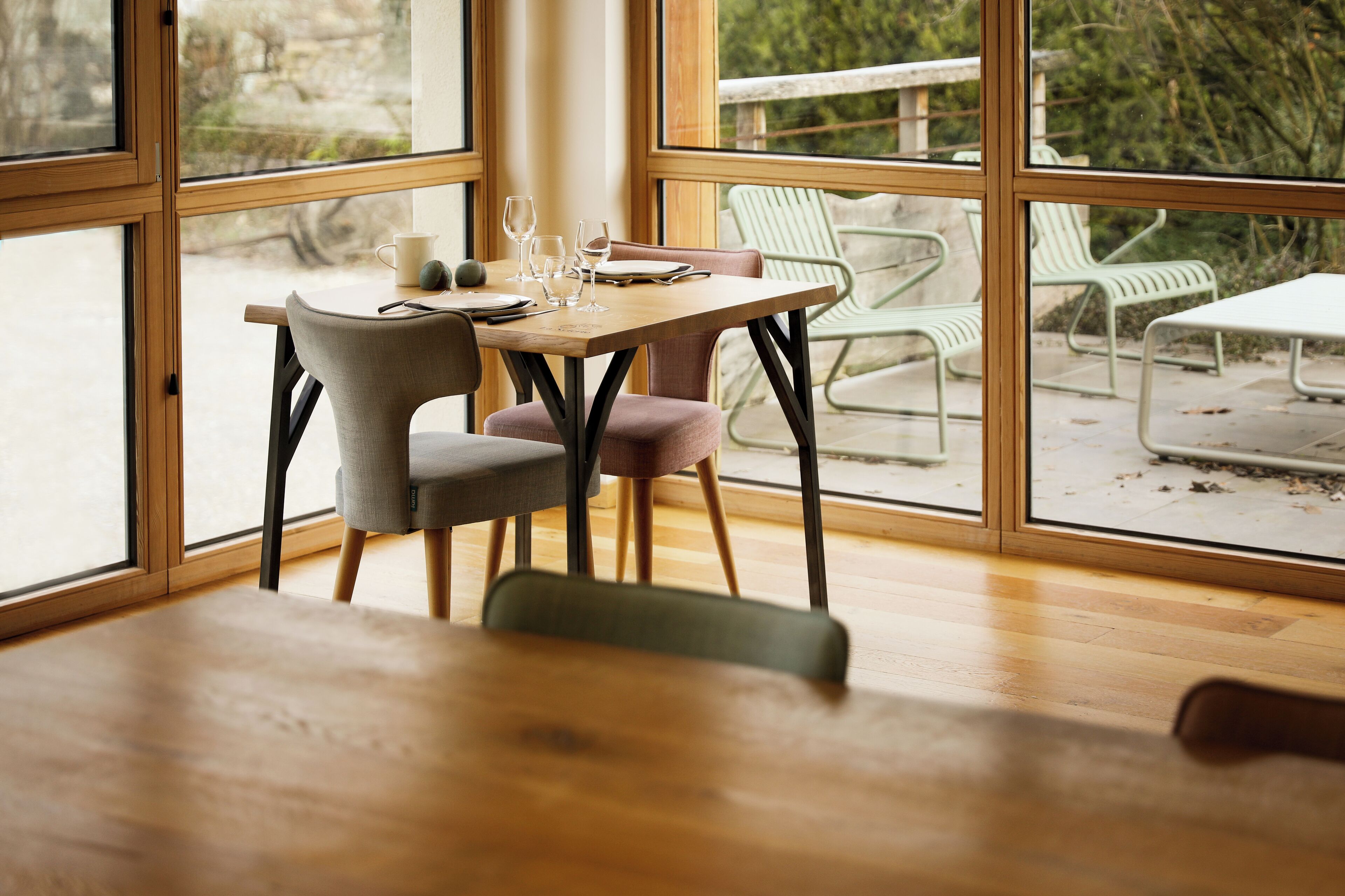 A dining area with a wooden table and chairs, large windows, and a view of outdoor seating.