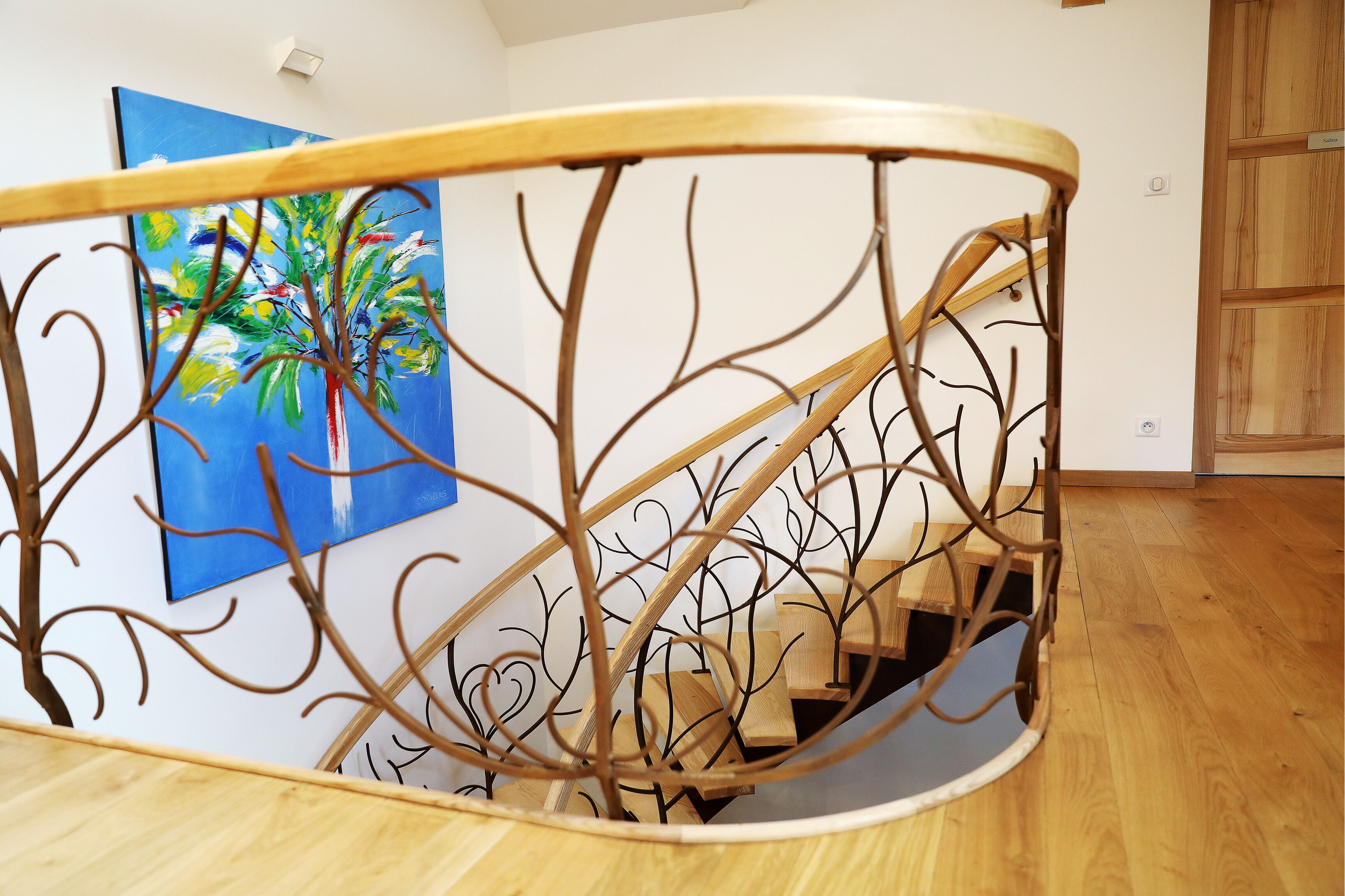 Una escalera de madera con barandilla de metal, un cuadro azul en la pared y una puerta de madera al fondo.
