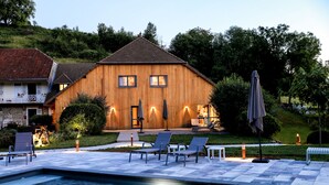 A wooden house with a swimming pool, outdoor seating, and a well-lit patio area. - Maison d'hôtes & Spa La Scierie (Salins-les-Bains)