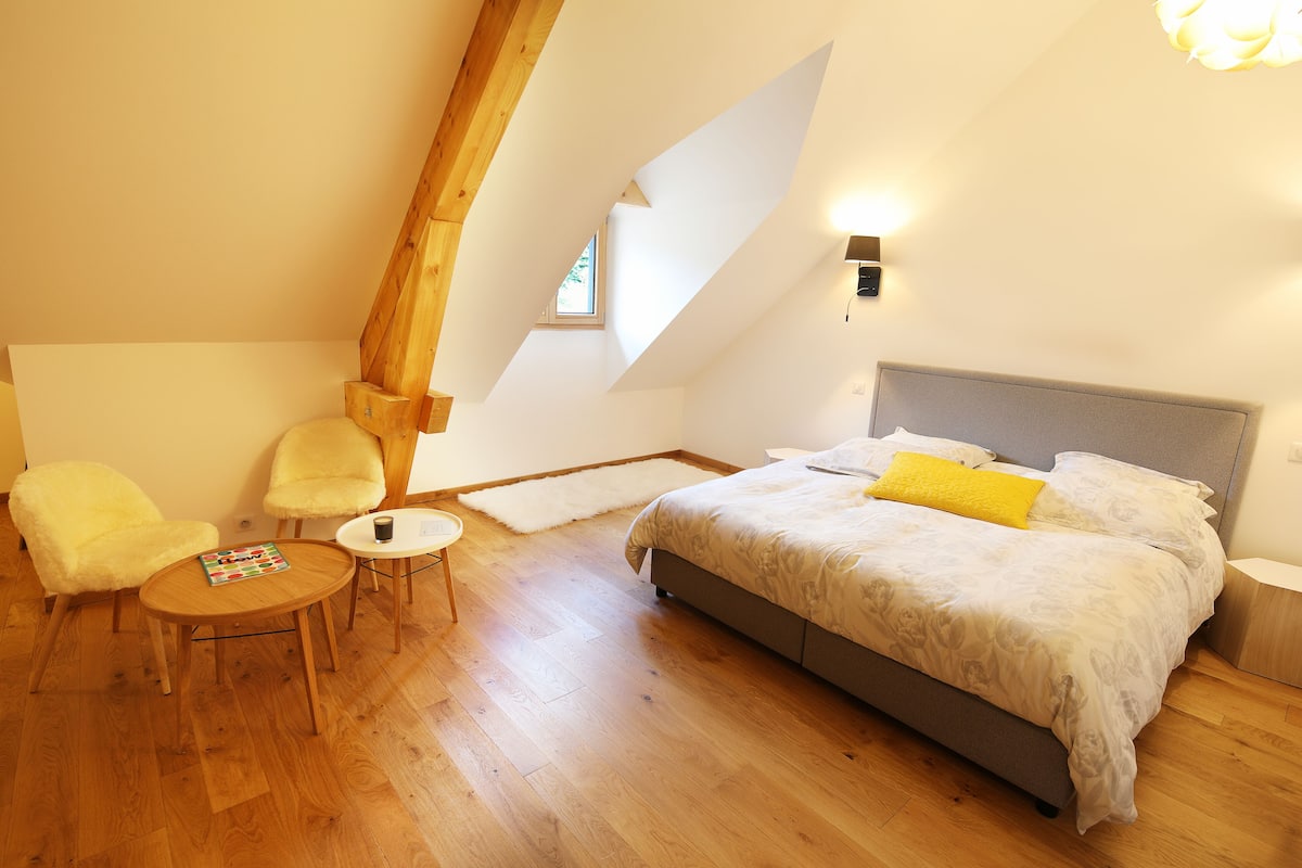 A bedroom with a bed, two chairs, a small table, and a window.