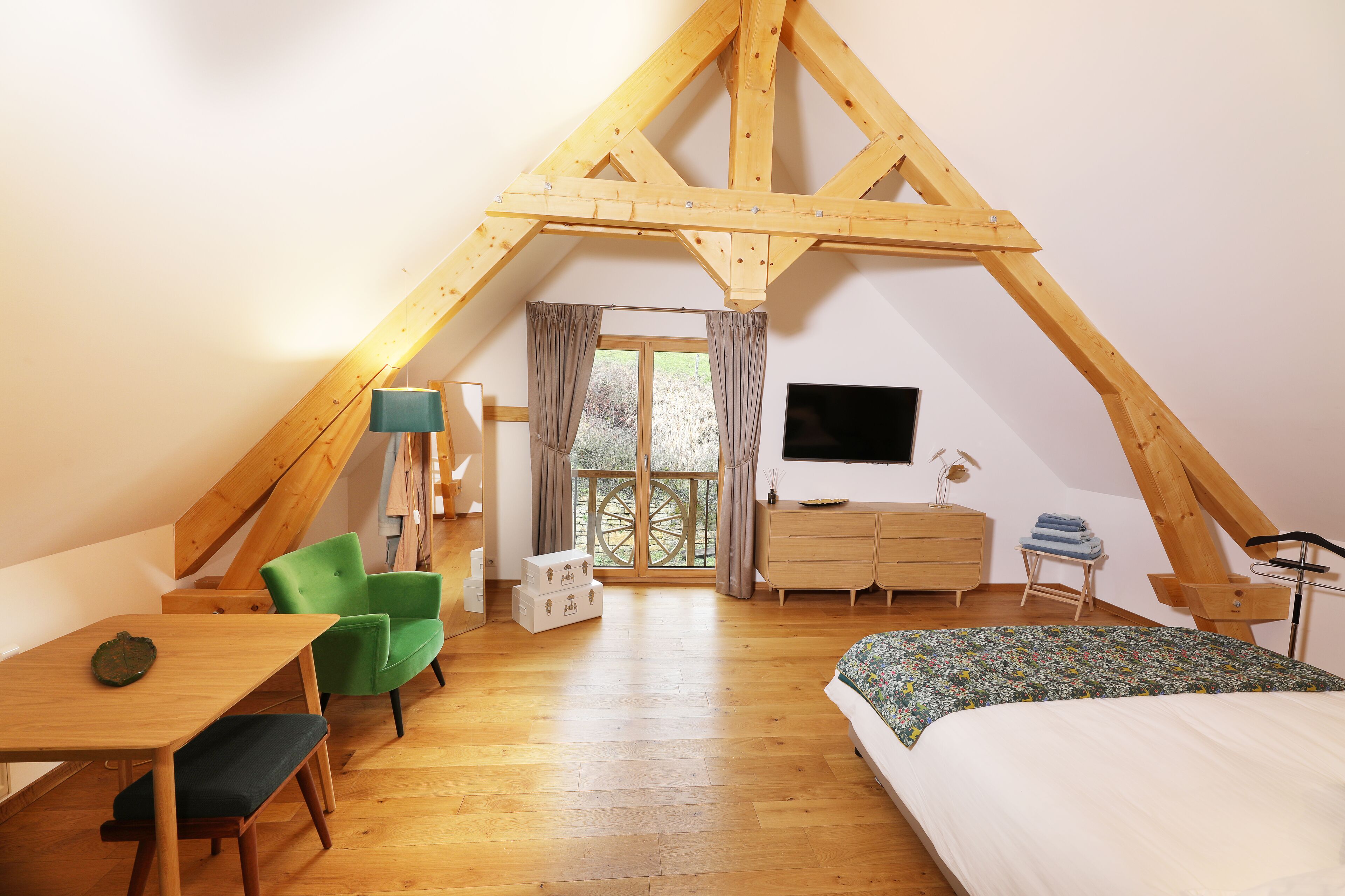 Une chambre confortable située sous les combles, avec un plafond en bois, un lit, un bureau, une chaise, une commode et un téléviseur.