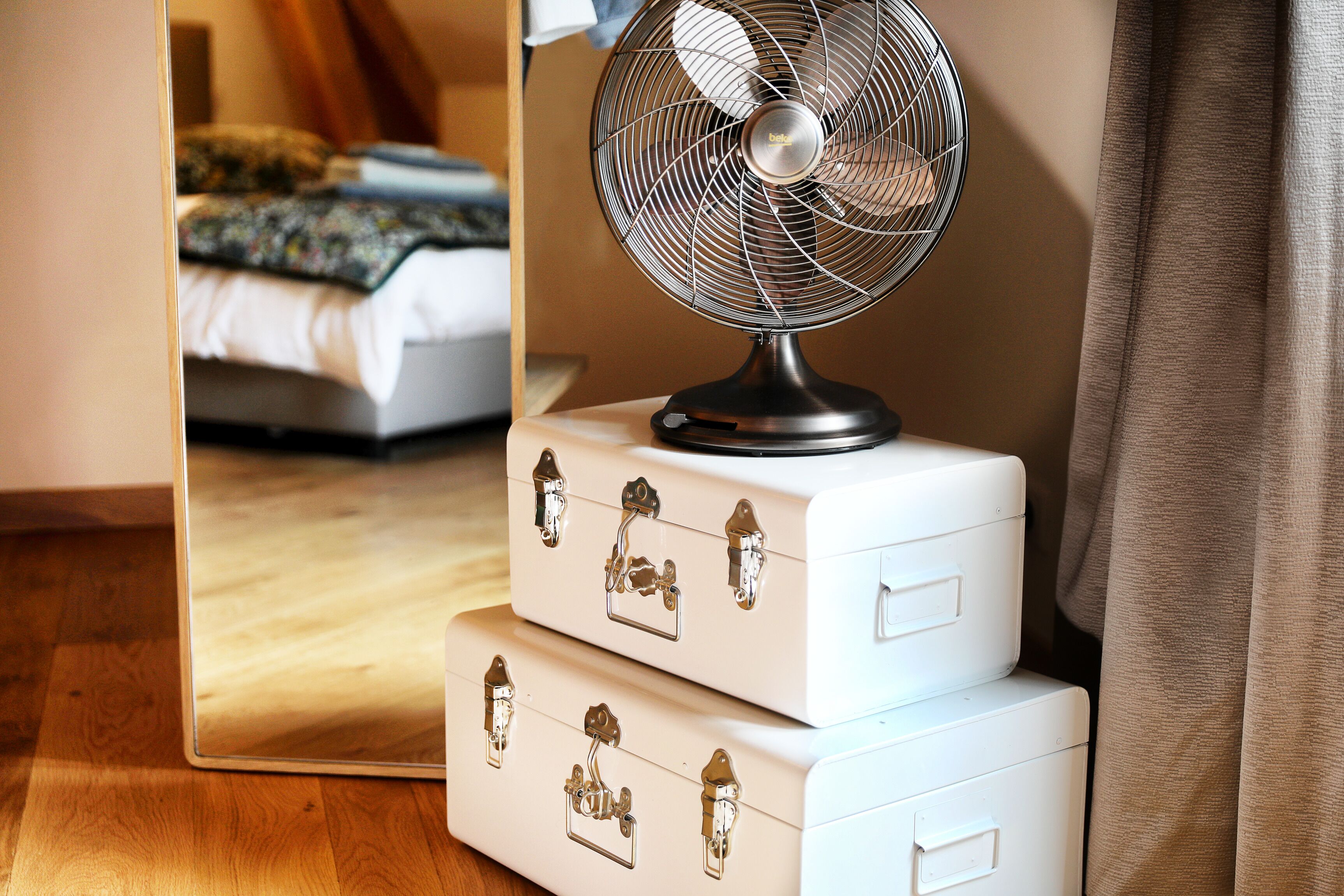 Een kamer met een bed, een ventilator en een spiegel die een deel van de kamer weerspiegelt.