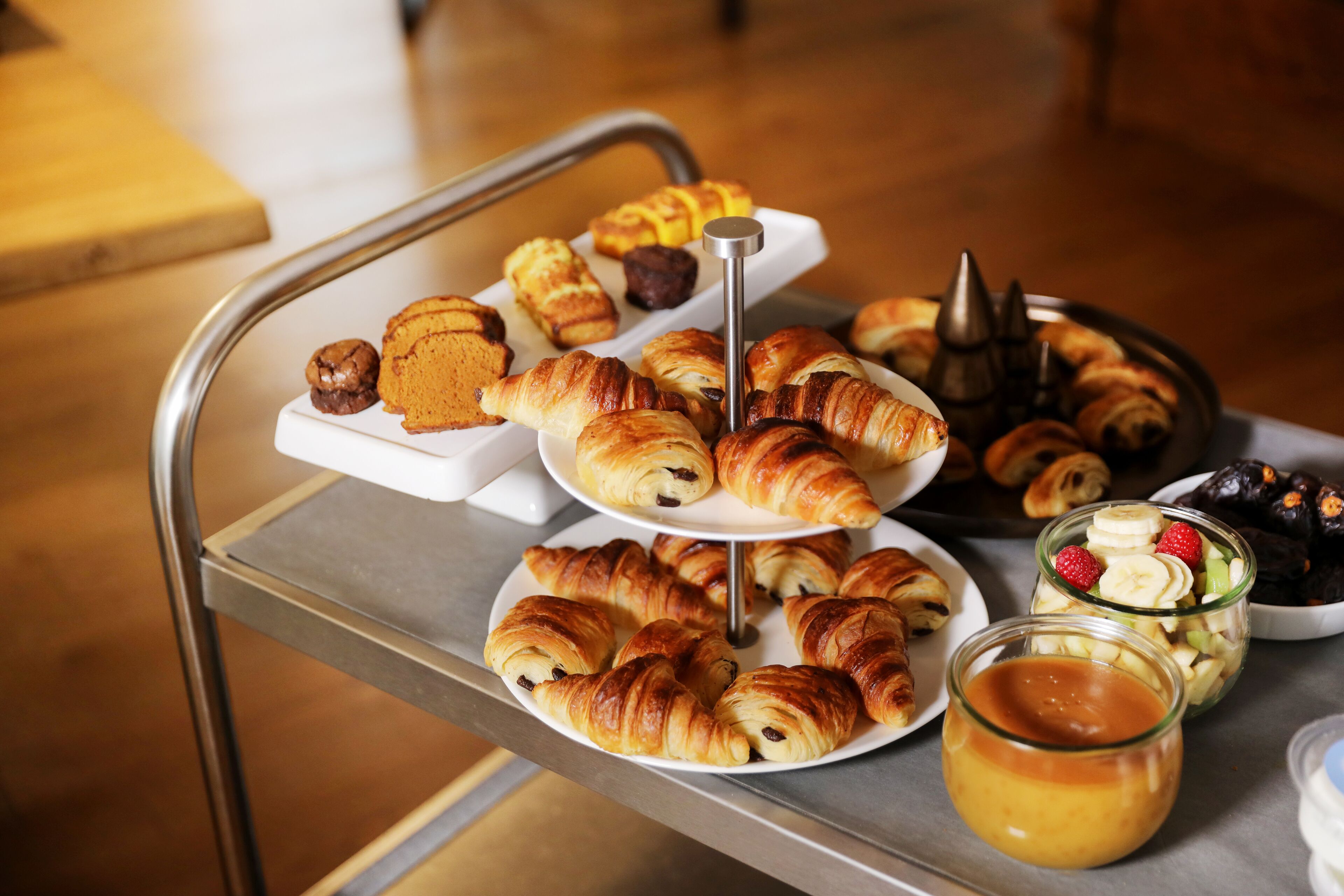 Un plateau contenant un assortiment de viennoiseries et de desserts, notamment des croissants et des muffins, présenté sur un présentoir en métal.