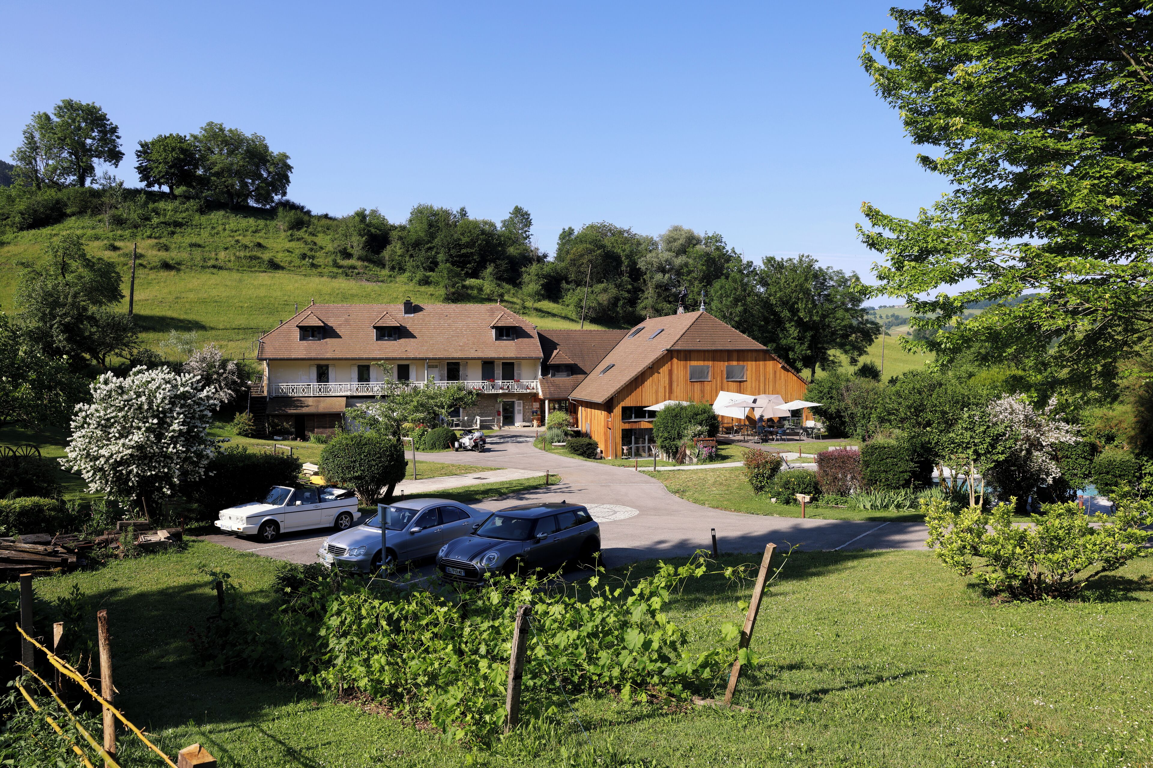 A hotel with a main building and a smaller annex, surrounded by lush greenery and parked cars.