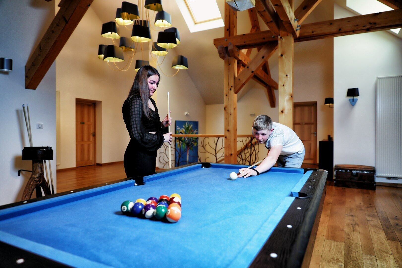 A pool table in a room with wooden beams and hanging lamps.