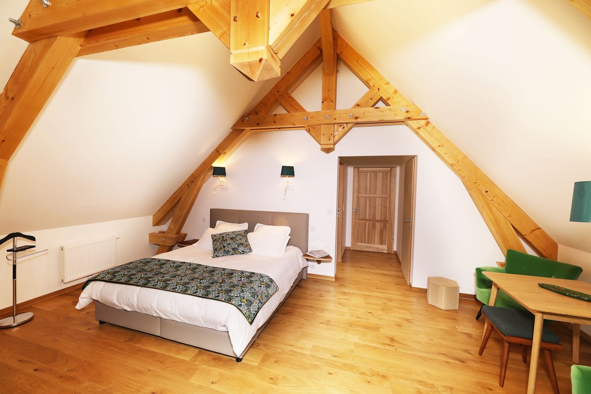 A bedroom with a sloped ceiling, a bed, a bedside table, a chair, and a small table with a lamp.