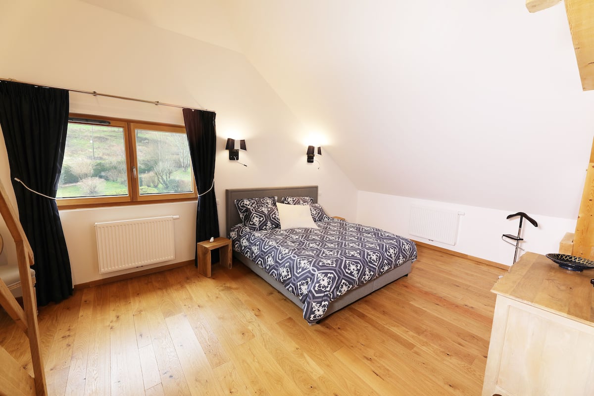 A bedroom with a bed, a window with curtains, a radiator, and a wooden floor.