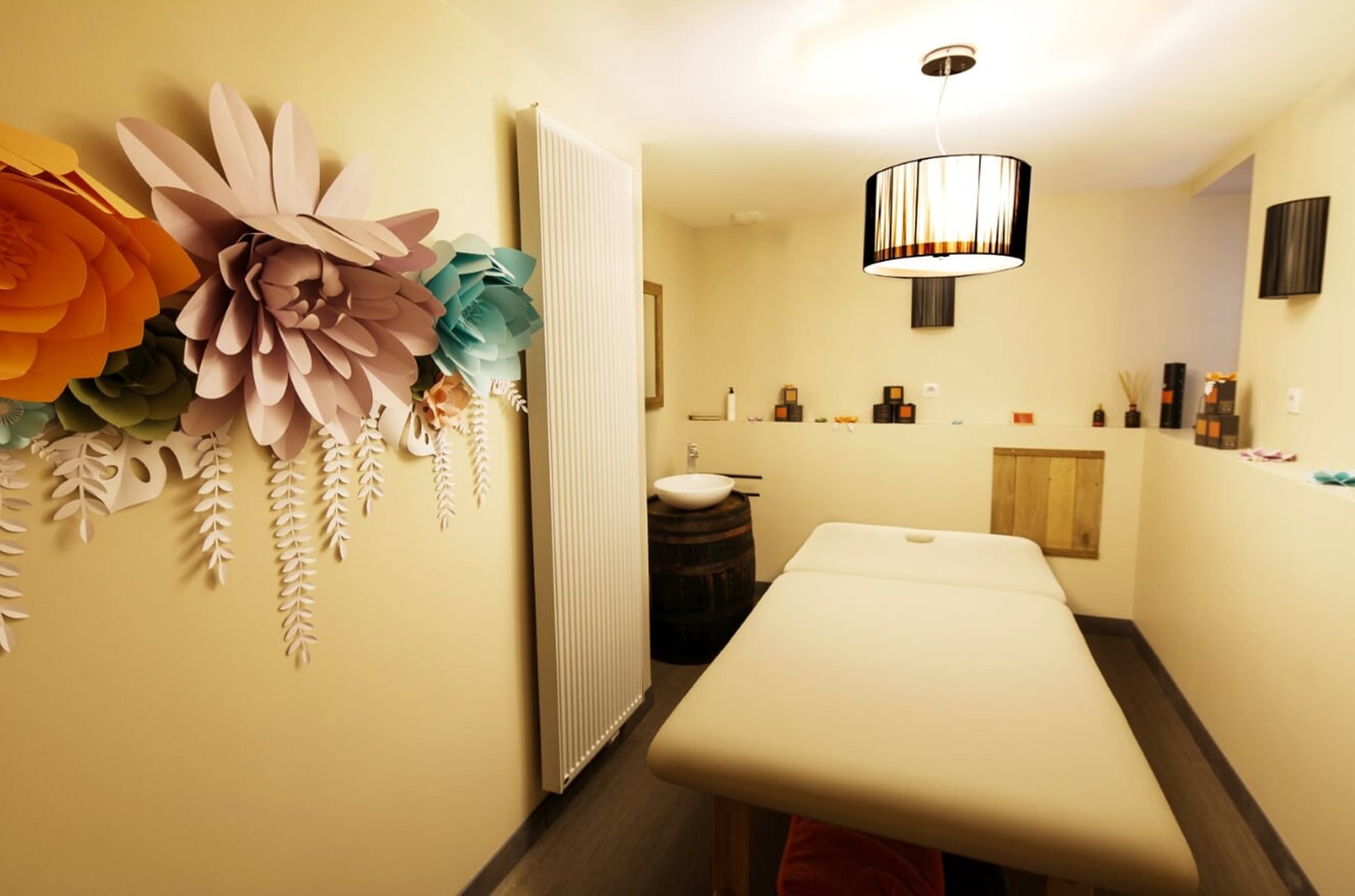 Um quarto com mesa de massagem, radiador, pia e flores de papel decorativas na parede.