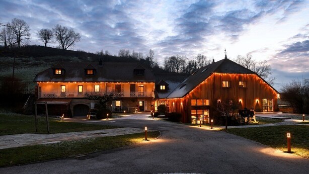 A large, rustic barn-style building with multiple windows and a covered porch, surrounded by a paved driveway and a cobblestone path. - Maison d'hôtes & Spa La Scierie (Salins-les-Bains)