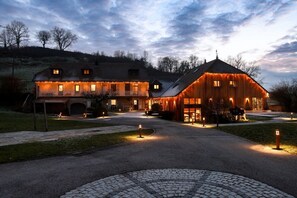 A large, rustic barn-style building with multiple windows and a covered porch, surrounded by a paved driveway and a cobblestone path. - Maison d'hôtes & Spa La Scierie (Salins-les-Bains)
