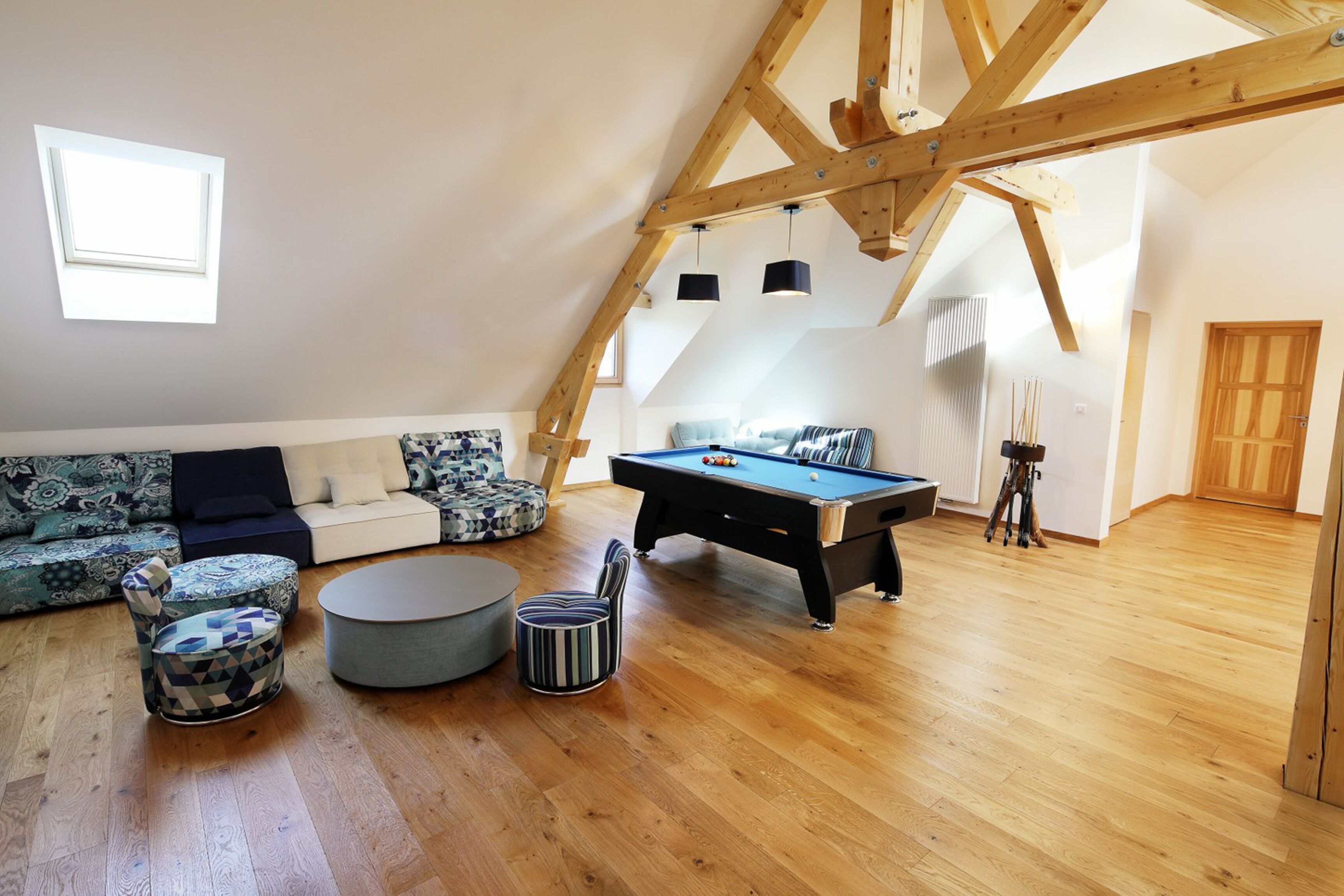 Ein großzügiges Loft mit Billardtisch, einer Sofagarnitur und einer Holzbalkendecke.
